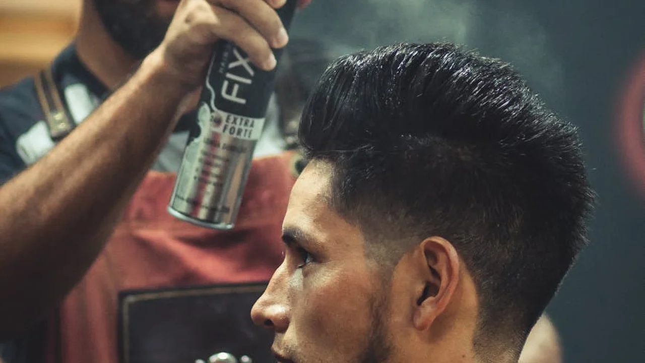 Hairstylist applying hair spray to a groomed man's hair
