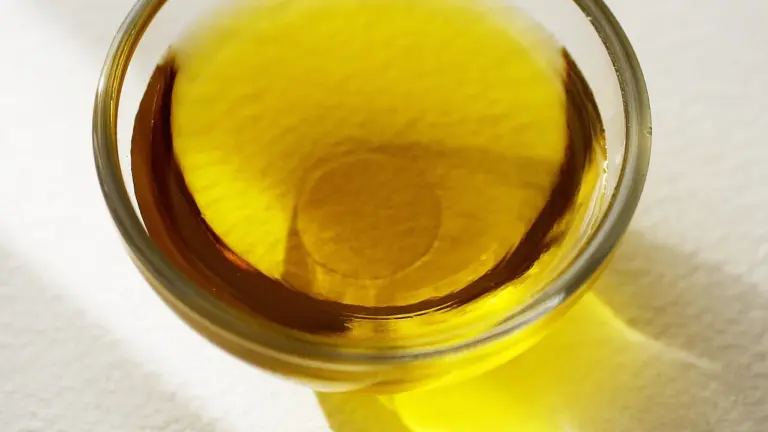 Close-up of a glass bowl filled with golden MCT oil on a light surface.