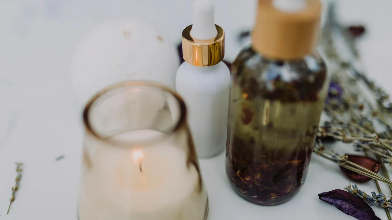 Skincare bottles, a dropper, and a candle on a soft, neutral surface, suggesting mink oil's use in personal care for skin and hair.