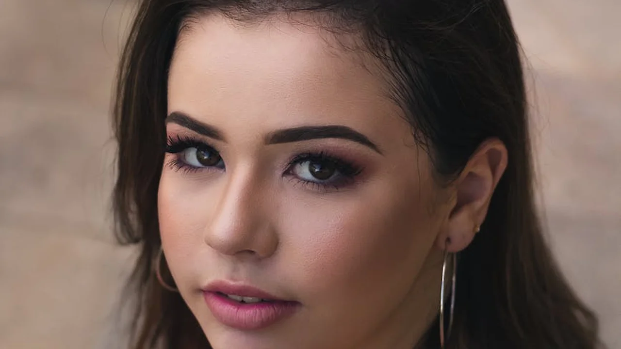Close-up portrait of a woman with dark hair and hoop earrings, wearing makeup