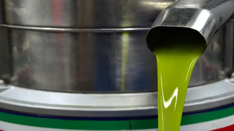 Bright green oil pouring from a stainless steel dispenser, illustrating natural oils used for nail care.