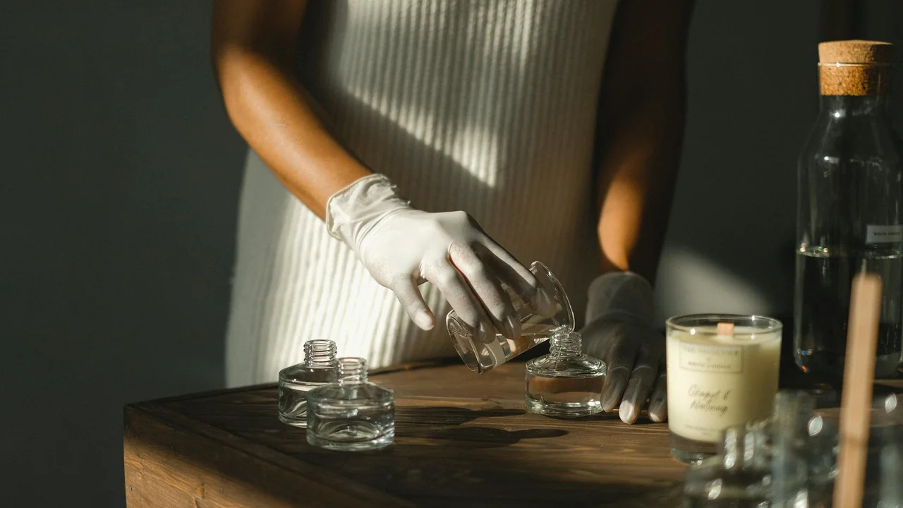 Person wearing gloves arranging small glass jars on a wooden table, preparing neem oil solution for plant pest control