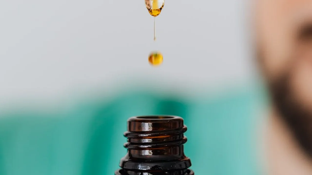 Close-up of a dropper releasing neem oil into a bottle with a blurred garden background.