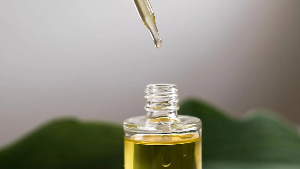 Dropper dispensing neem oil into a small glass bottle against a blurred green leaf background.