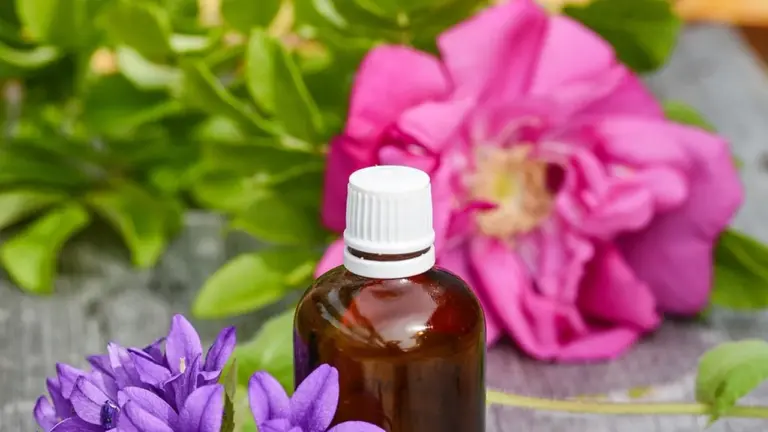 Brown bottle of essential oil on a wooden surface with purple and pink flowers, suggesting focus and stress relief in the workplace.
