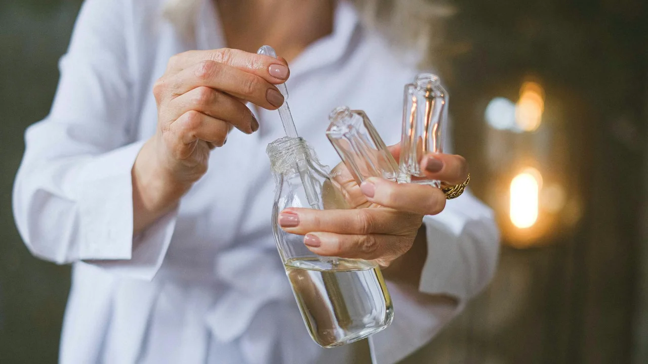 Person in white clothing holding glass bottles of essential oil with a dropper, in a calm office setting.