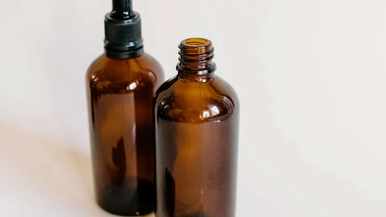 Two amber glass bottles of oil, one with a dropper cap and the other open, resting on a light surface