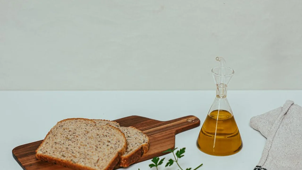 Bottle of oil beside slices of bread on a wooden cutting board