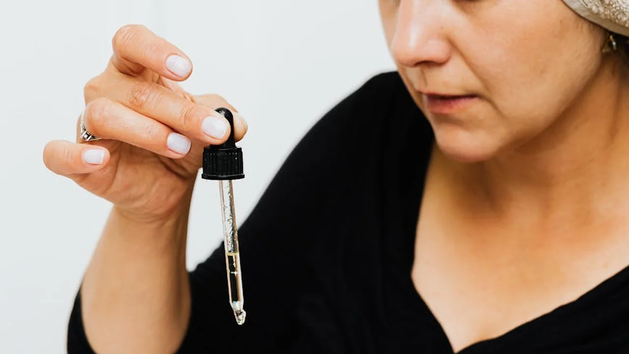Close-up of a hand holding a glass dropper filled with skincare oil, preparing to dispense a drop
