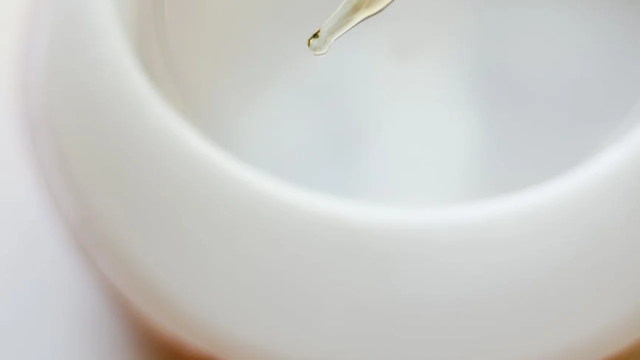 Close-up of a droplet of oil being poured into a white liquid, showing the interaction between oil and water.