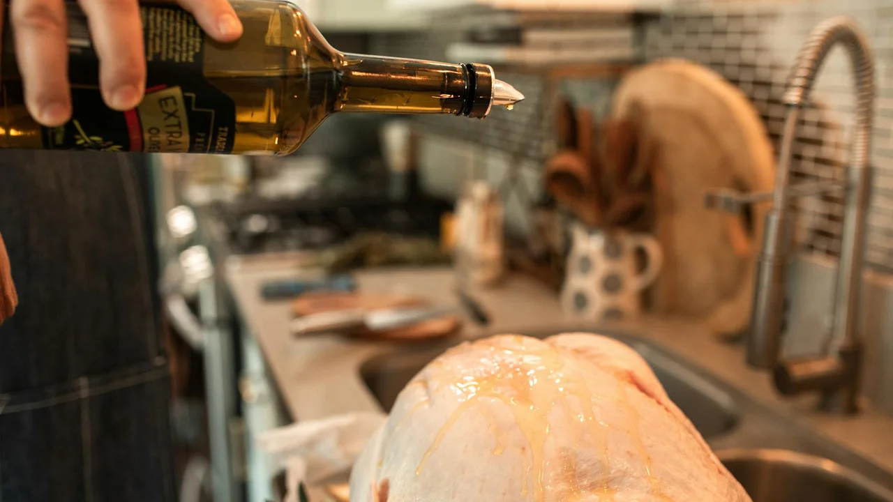 Person's hand pouring olive oil from a bottle into a kitchen setup to start emulsifying mayonnaise.