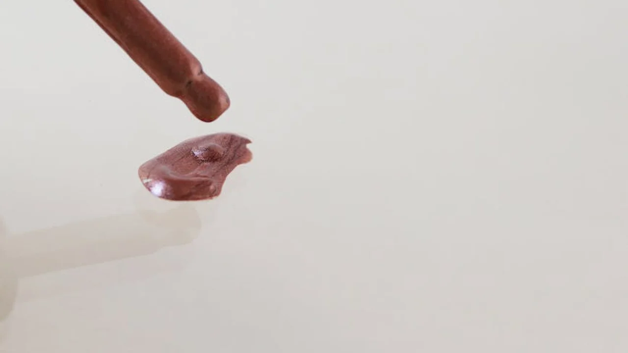 Close-up of a finger with a small oil drop on the fingertip against a pale background