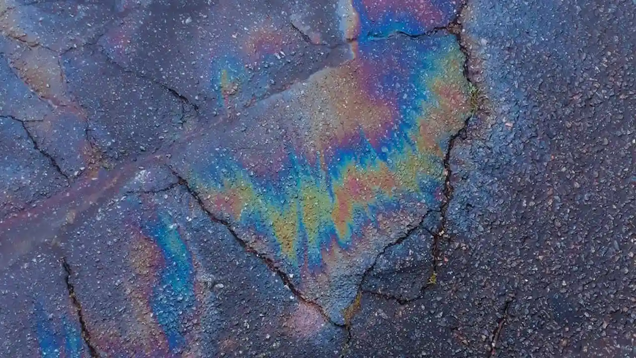 Cracked concrete surface with a rainbow iridescent oil sheen.