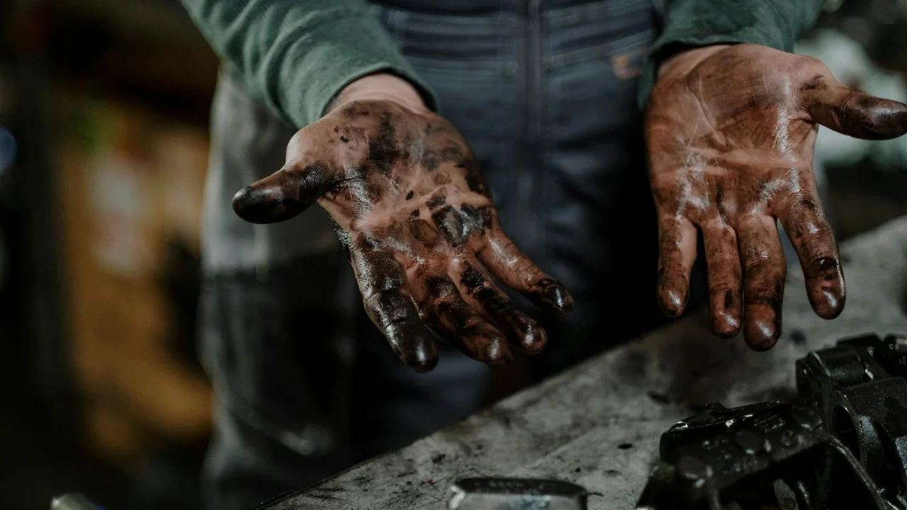 Close-up of dirty hands with oil stains over a work surface, illustrating the need for preventive cleaning habits.