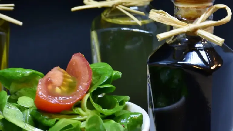 Fresh greens and a tomato salad beside glass bottles of oil with cork stoppers, set against a dark background.
