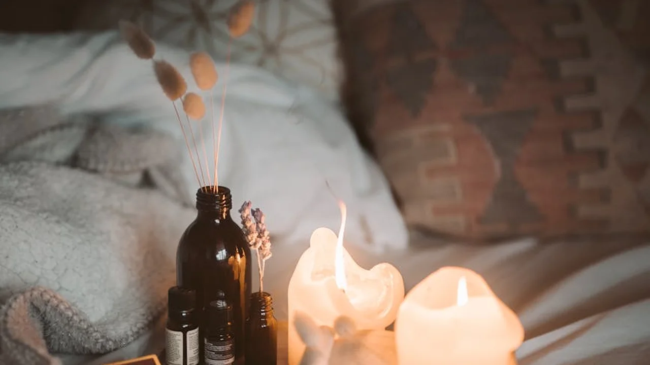 Brown glass bottles of facial oils with dried plant sprigs and warm candlelight on a soft, textured surface.