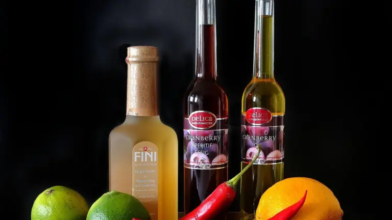 Assorted cooking oil bottles with citrus fruits and a red chili pepper on a dark background.
