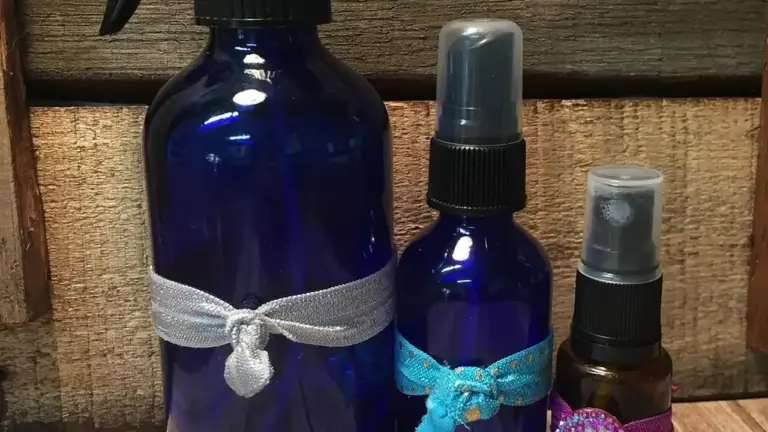 Three blue-glass spray bottles with decorative ribbons placed on a wooden background, representing scalp care oils.