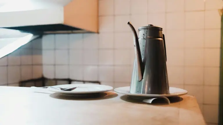 Metal oil can with a long spout sits on a kitchen counter against a tiled backsplash.