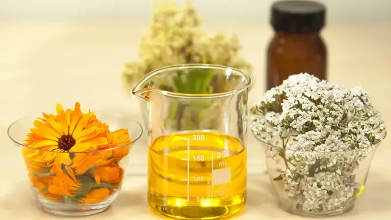 Beaker filled with yellow oil on a lab bench, flanked by orange flowers and a white floral arrangement.
