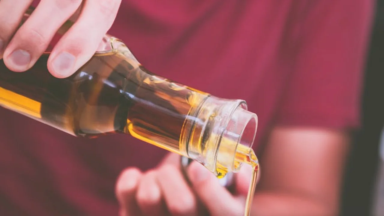 Close-up of a hand pouring oil from a bottle, with a blurred background