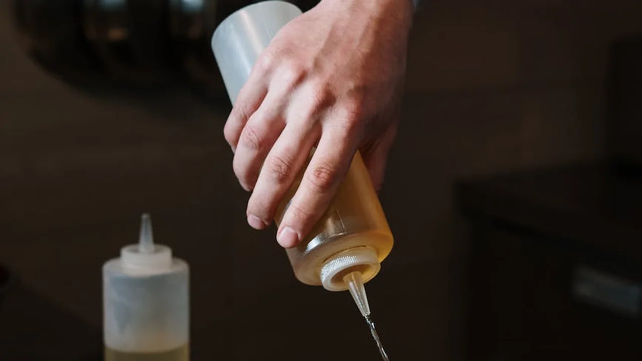 Close-up of a hand squeezing a bottle of cooking oil, with another bottle visible in the background.