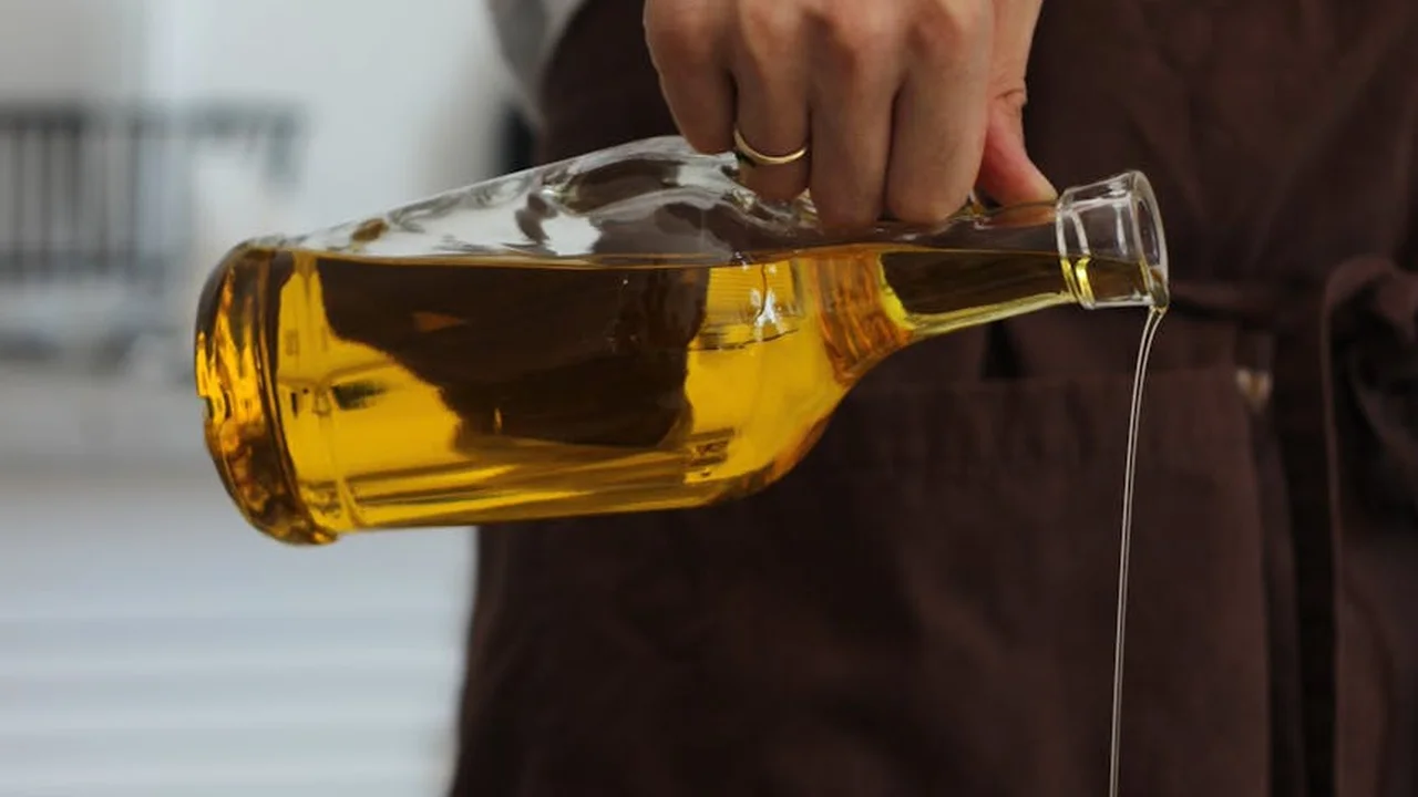 Close-up of a hand pouring golden olive oil from a glass bottle