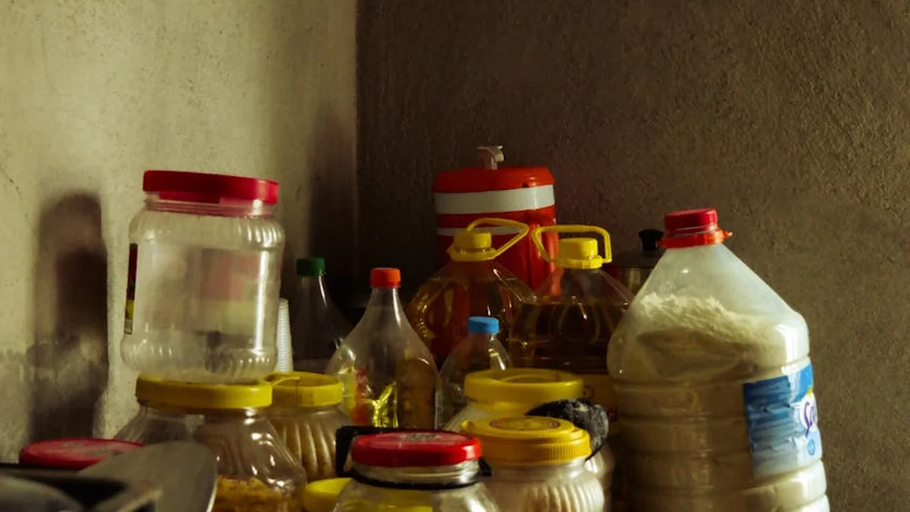 Assorted bottles and jars of cooking oils on a cluttered kitchen shelf.