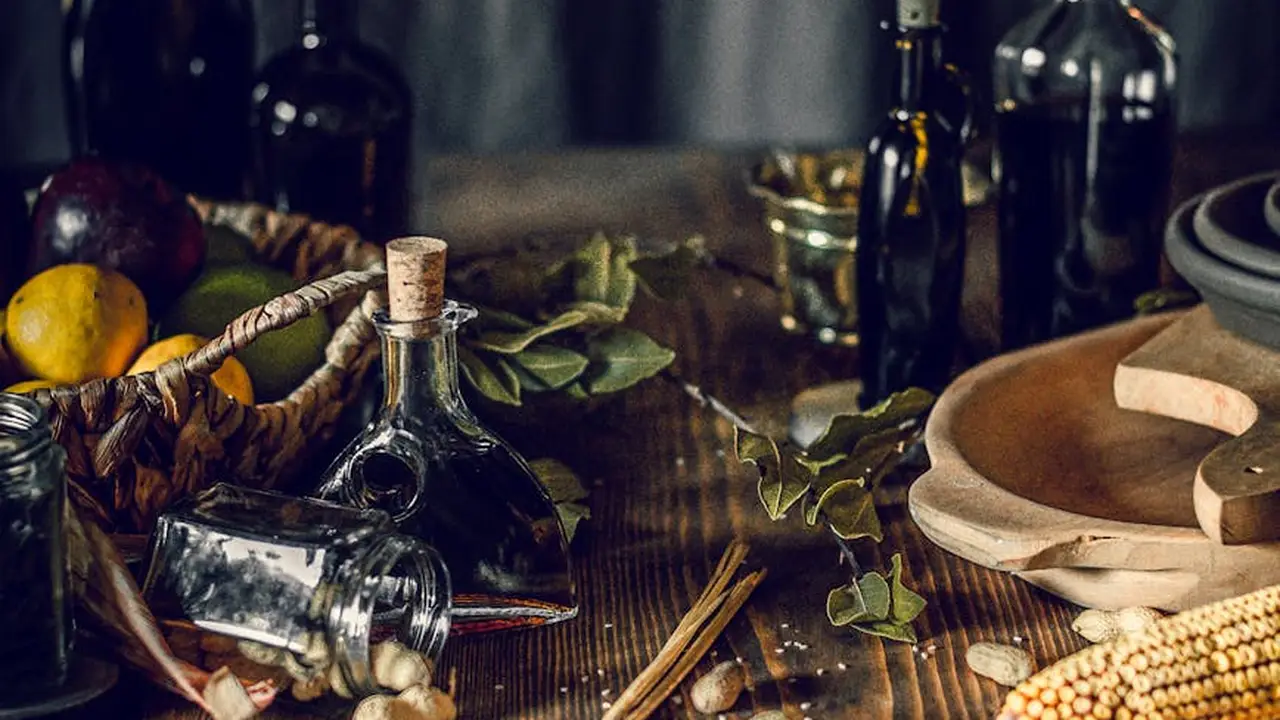 Assorted oil bottles on a rustic wooden table with herbs and a corked bottle, illustrating a kitchen storage scene.