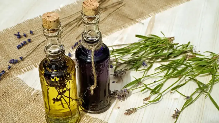 Two glass bottles of essential oil with rosemary and lavender sprigs on a beige fabric surface