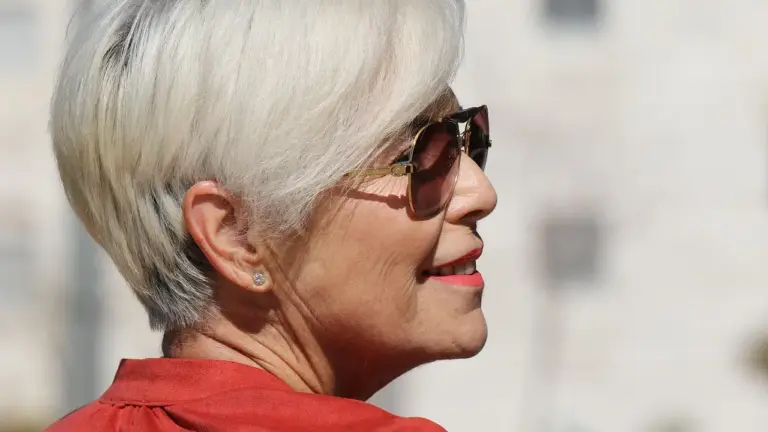 Side profile of an older woman with short white hair wearing sunglasses outdoors.