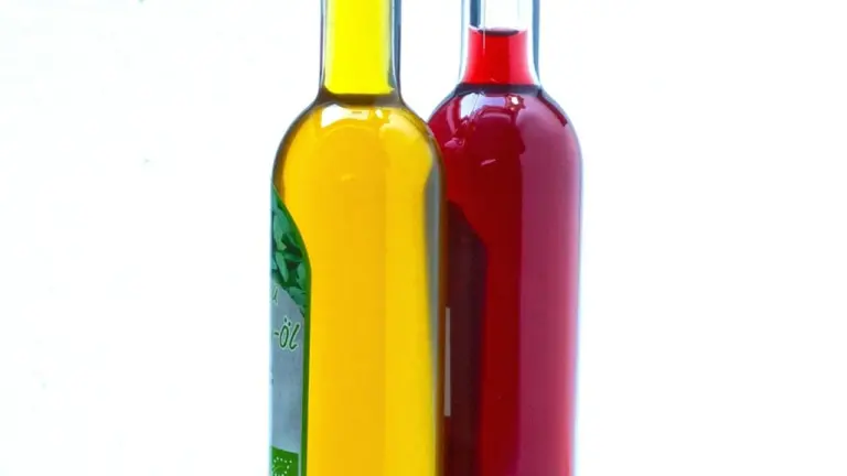 Two bottles of oil on a white background, one containing olive oil and the other a reddish oil