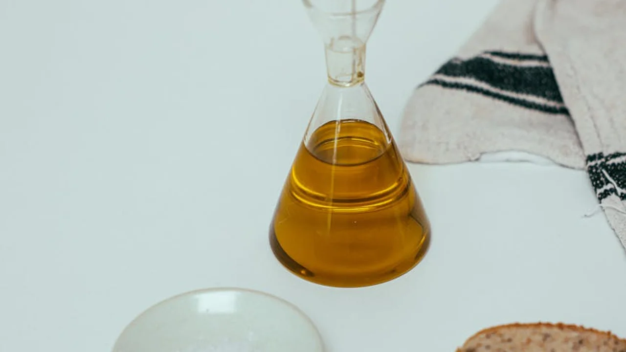 A glass bottle of olive oil on a light counter with a striped towel in the background.