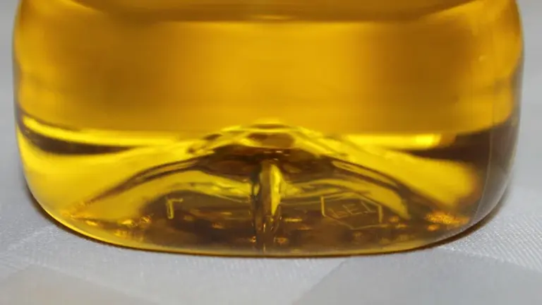 Close-up of a glass bottle containing golden olive oil with reflections on a light surface.