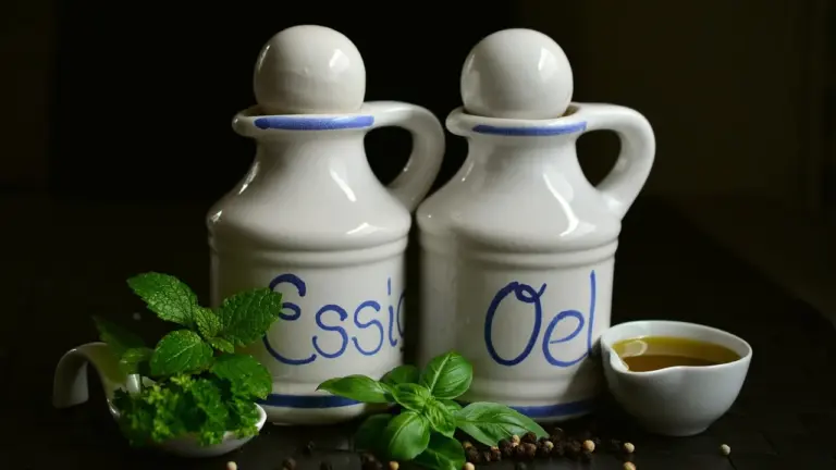 Two ceramic oil bottles with a small dish of oil and fresh herbs on a dark wooden surface