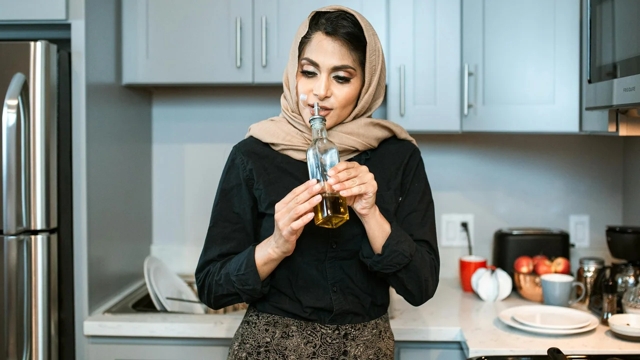 Person wearing a beige headscarf holding a bottle of olive oil in a modern kitchen