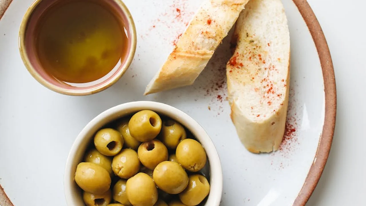 Small bowl of olive oil with green olives and slices of bread on a white plate