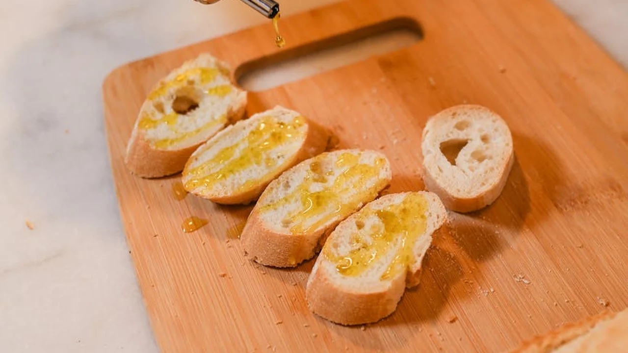 Sliced baguette on a wooden cutting board with olive oil being drizzled from a dropper.