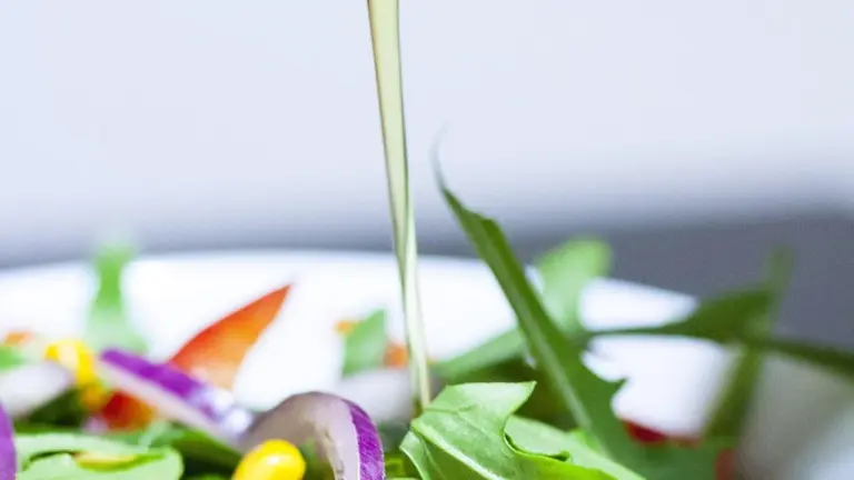 A stream of olive oil being poured onto a colorful plate with greens and vegetables, illustrating oil as a flavor base for snacks.