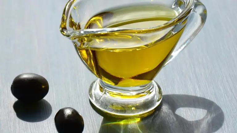 Close-up of olive oil in a glass cruet with two black olives on a light, reflective surface