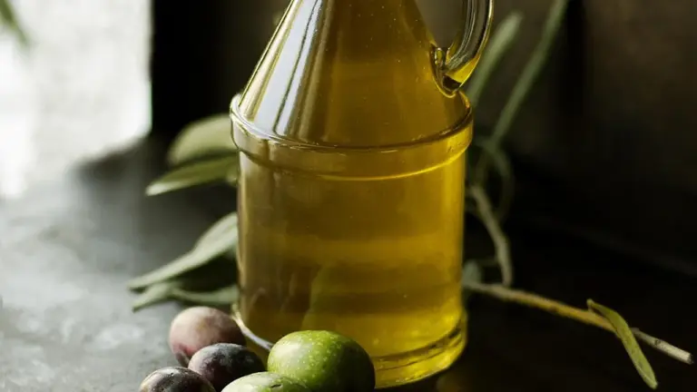 Olive oil in a glass bottle with olive leaves on a dark surface
