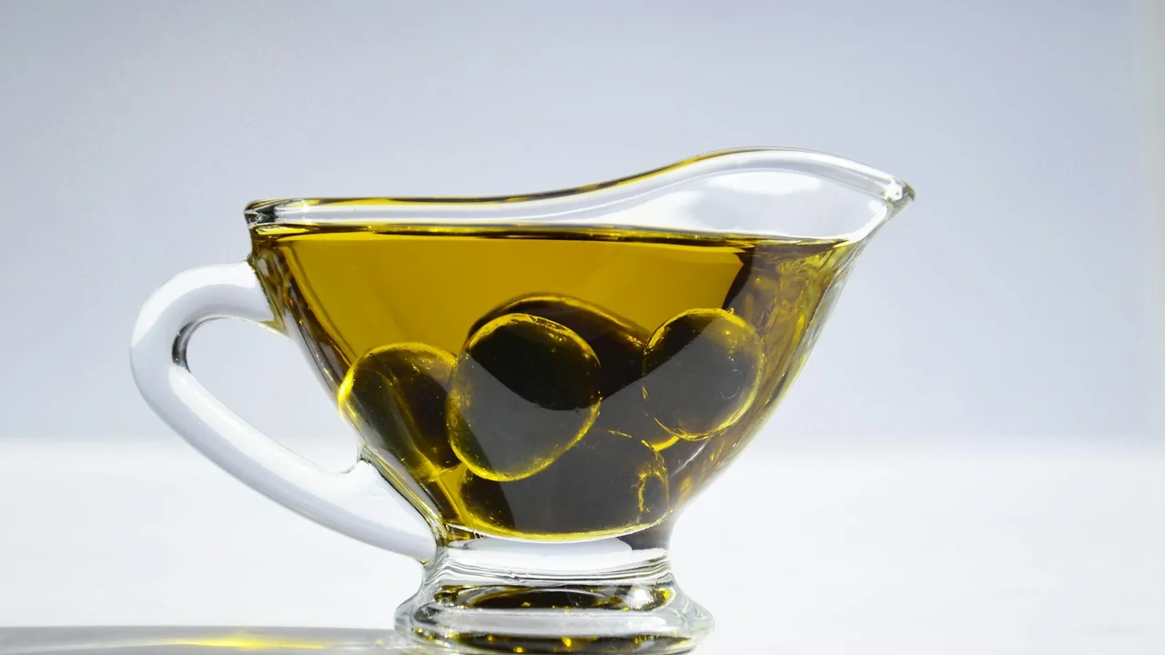 Glass cruet filled with olive oil on a pale background