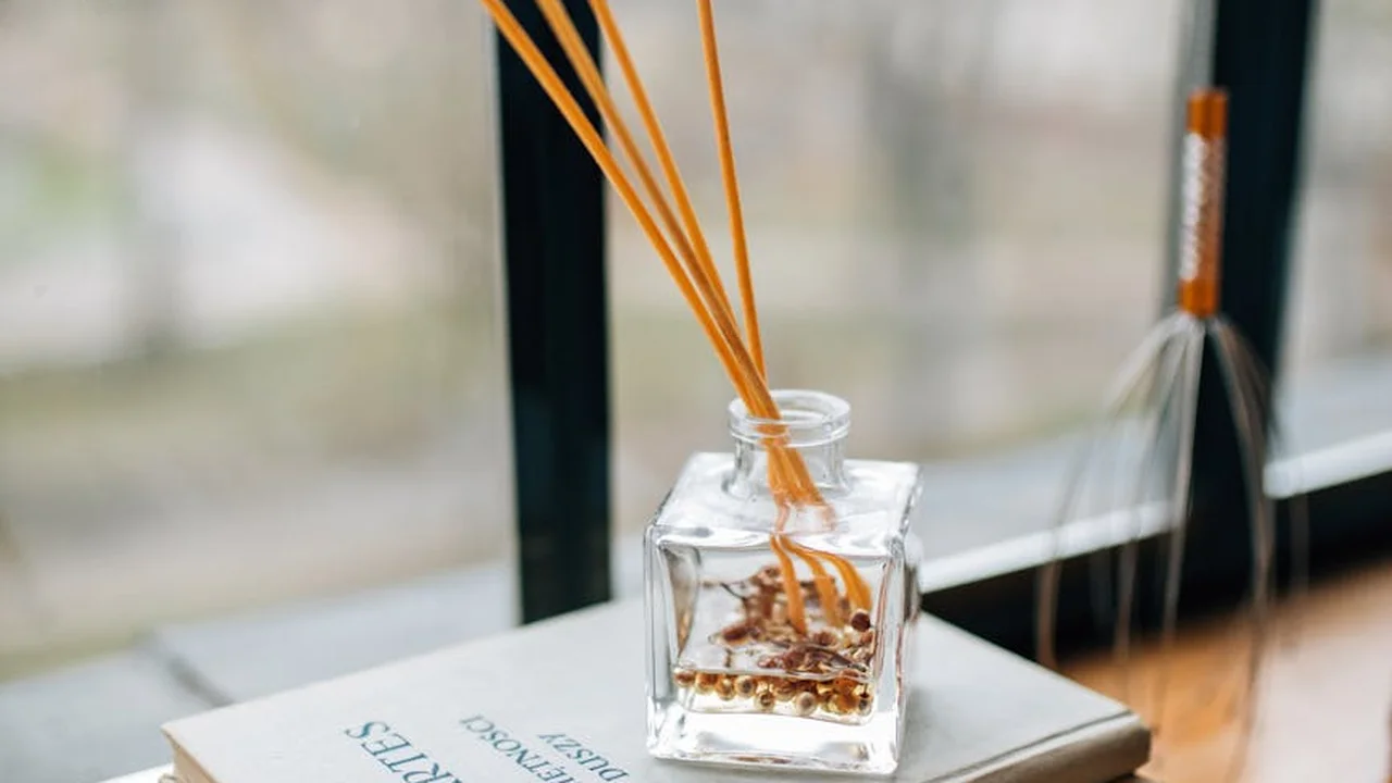 Reed diffuser with orange oil in a glass bottle on a windowsill.