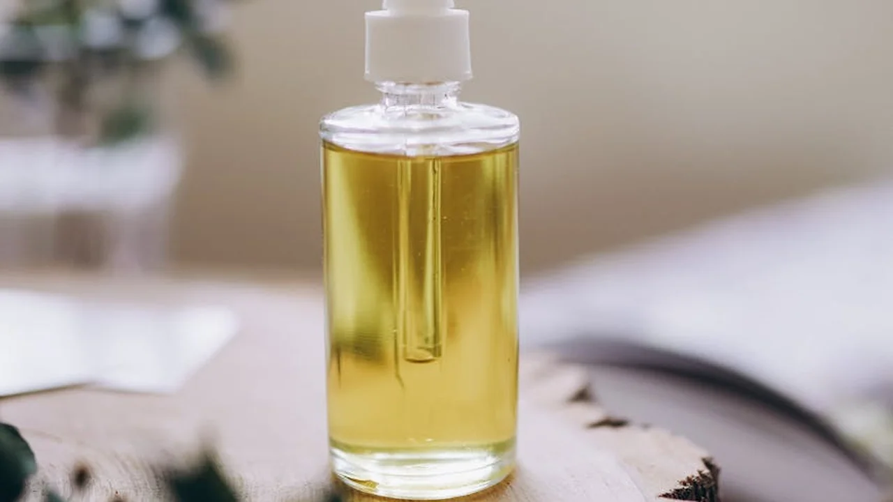 Clear glass bottle with a dropper cap containing golden oregano oil on a light surface.