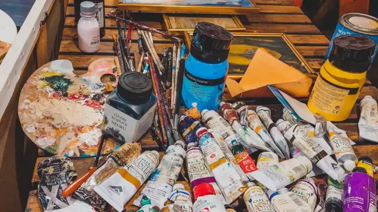 Assorted oil paints, brushes, and painting supplies scattered on a wooden table.