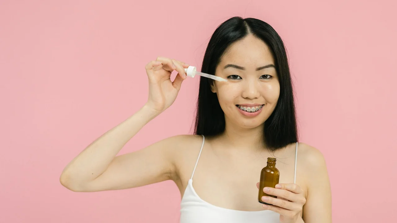Woman applying skincare oil with a dropper in front of a pink background, illustrating a patch test.