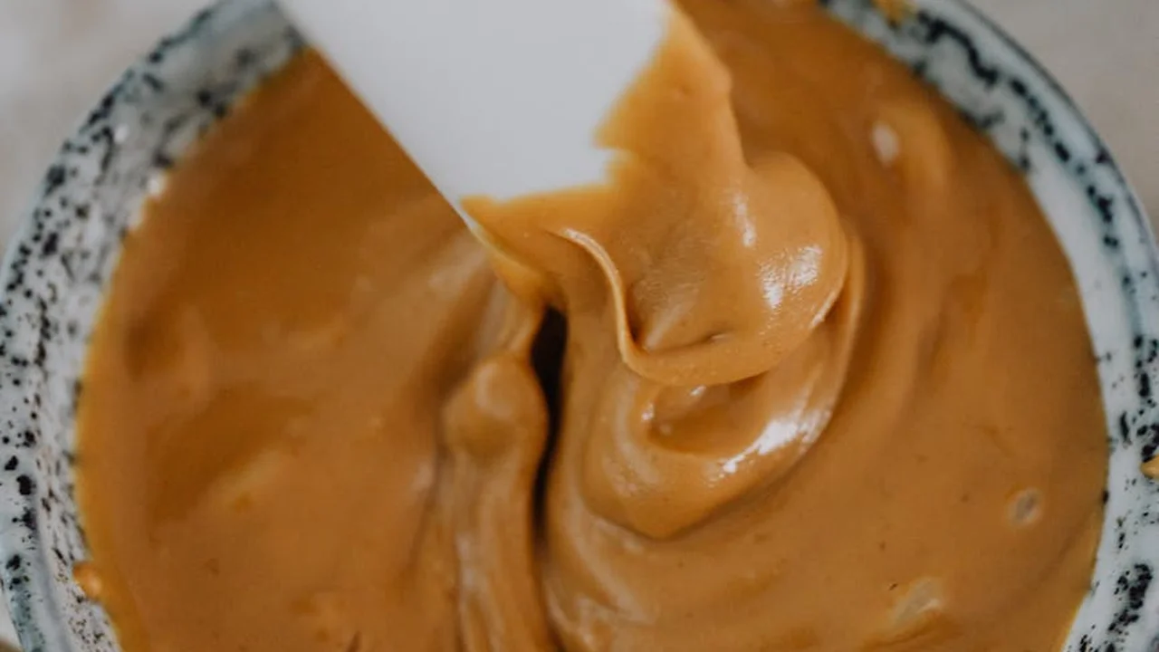 Close-up of creamy peanut butter swirled on a white spatula in a speckled bowl.