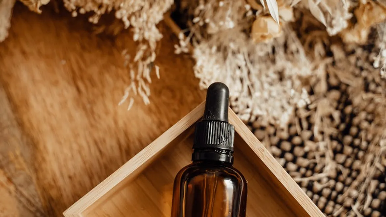 Brown glass dropper bottle of essential oil on a wooden tray with dried botanicals in the background.