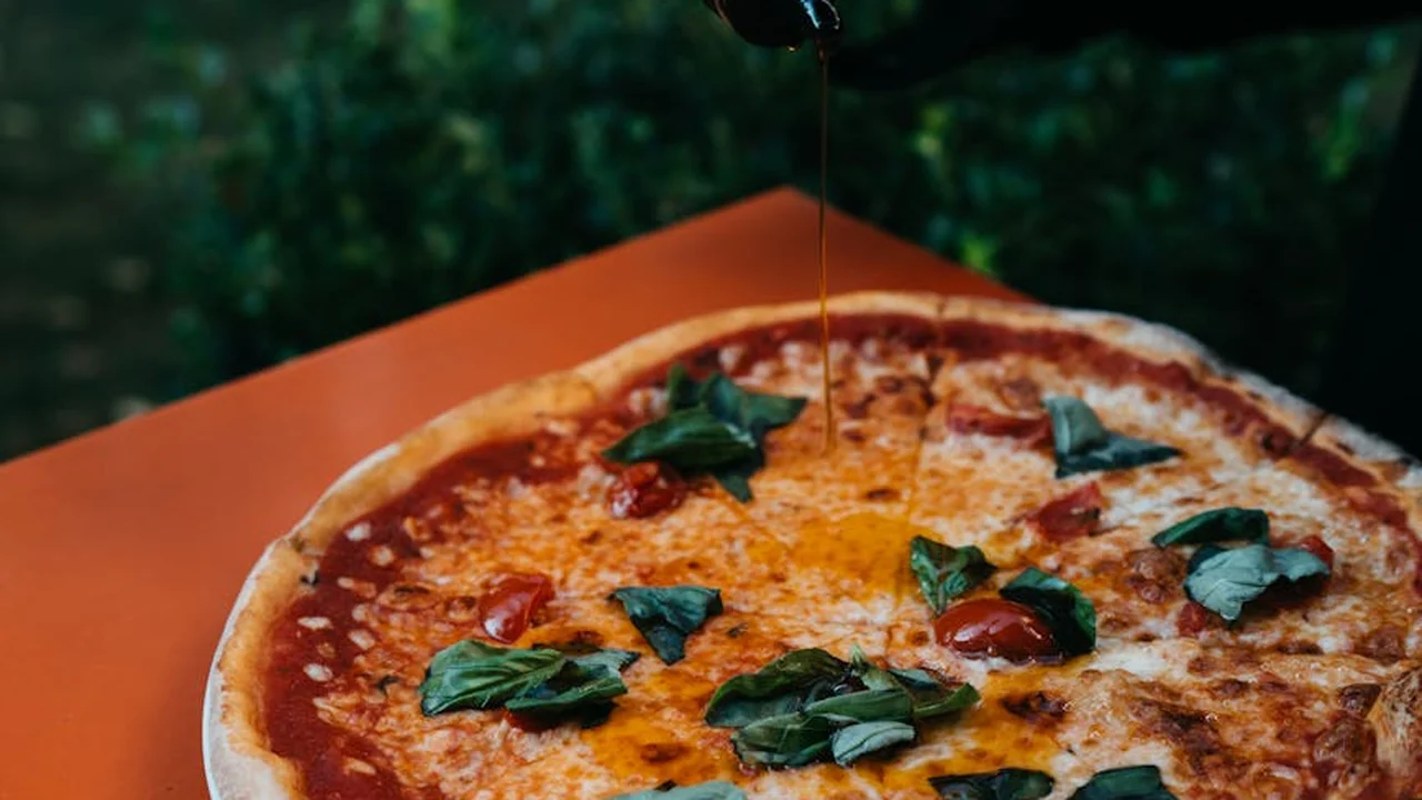 Pizza topped with fresh basil and melted cheese, with olive oil being drizzled on top.