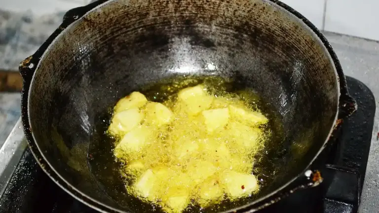 Cubed potatoes frying in hot oil in a dark, seasoned frying pan.